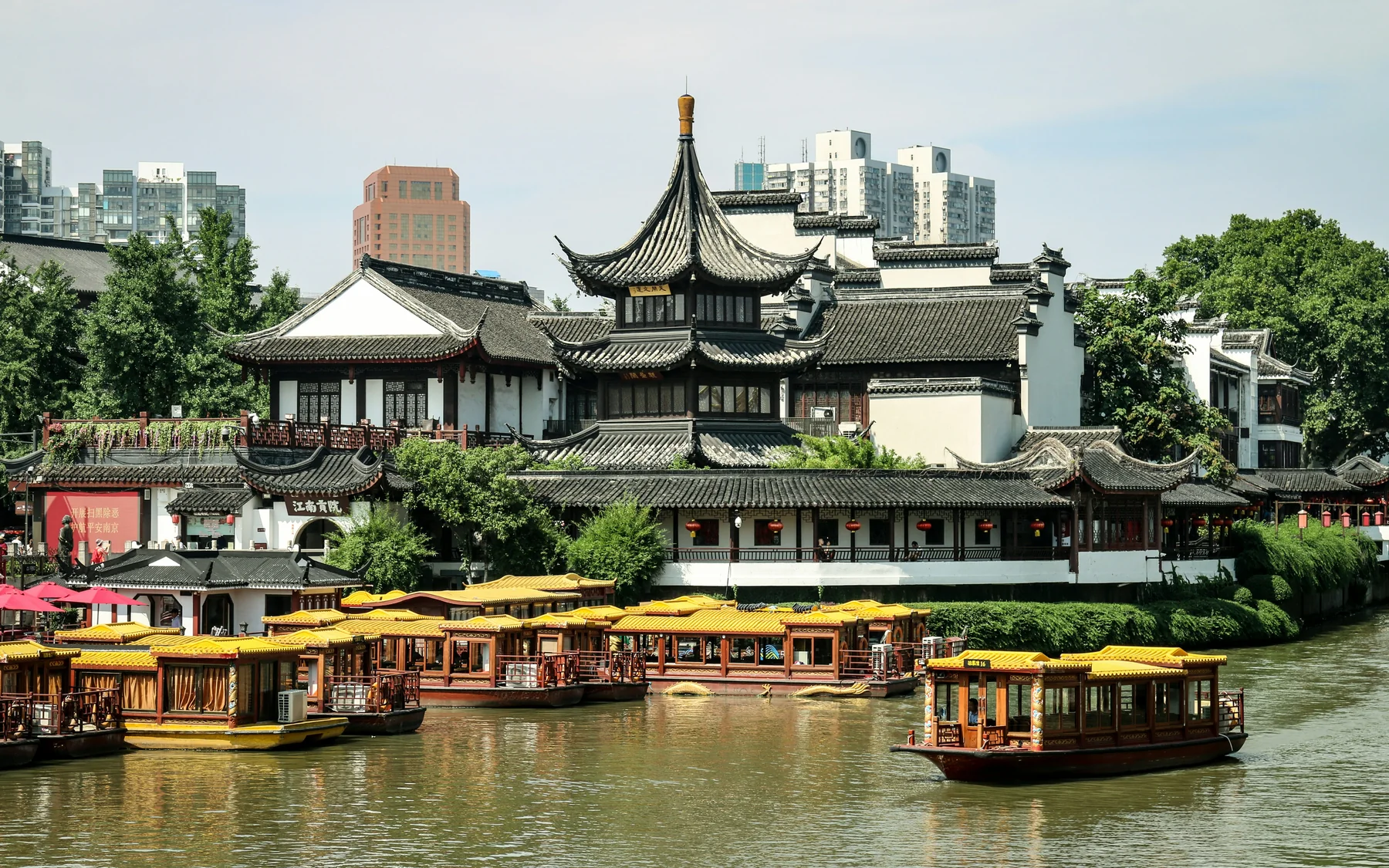 Yellow-roofed sightseeing boats on the Qinhuai River in front of traditional buildings in Nanjing's Confucius Temple district.