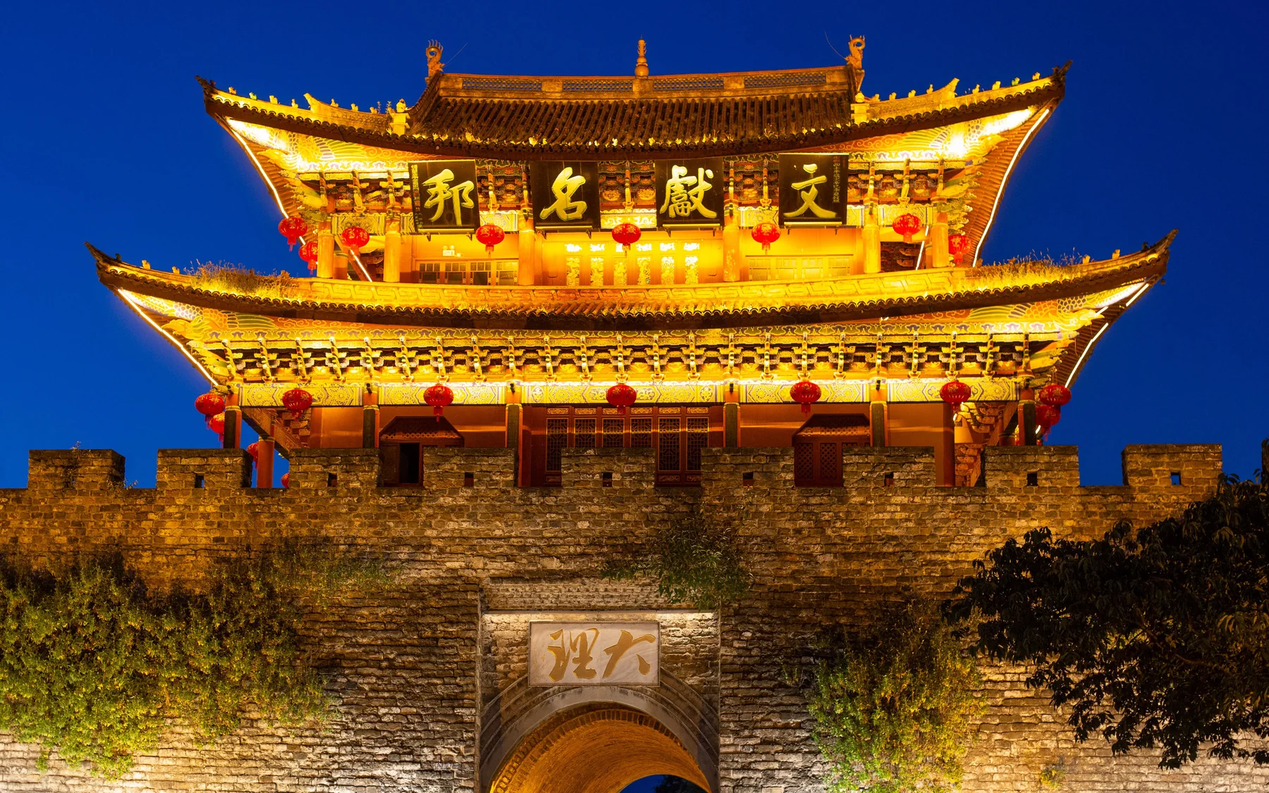 An illuminated historic gate of Dali Old Town glowing against the deep blue evening sky