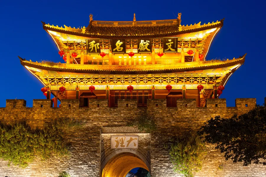 An illuminated historic gate of Dali Old Town glowing against the deep blue evening sky