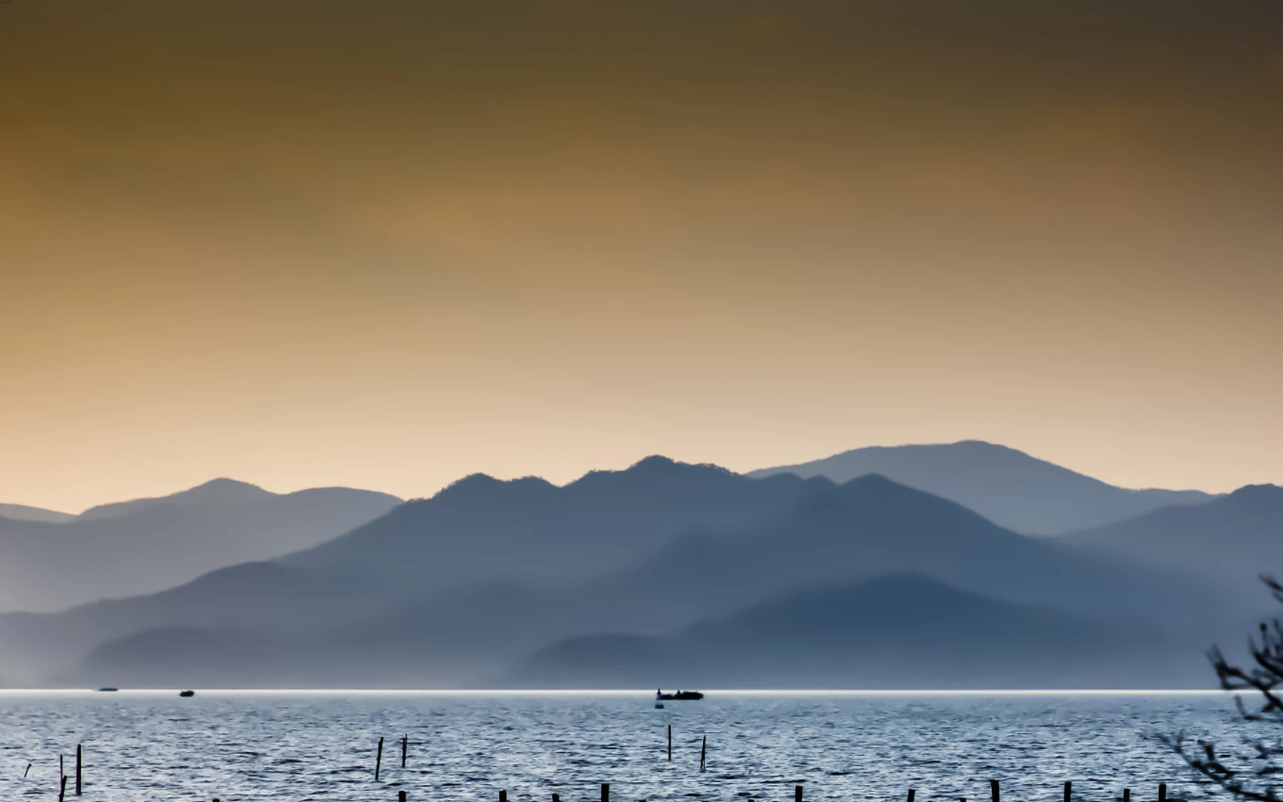 Layered mountains and a small boat beyond the reflective water of Dongqian Lake at dusk
