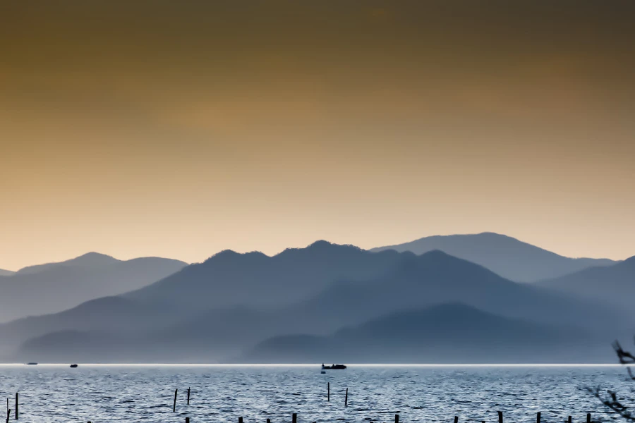Layered mountains and a small boat beyond the reflective water of Dongqian Lake at dusk