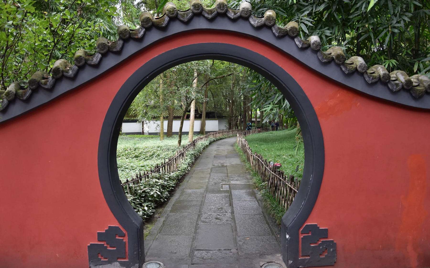 A red moon gate opening onto the bamboo garden path at Du Fu Thatched Cottage Museum in Chengdu.