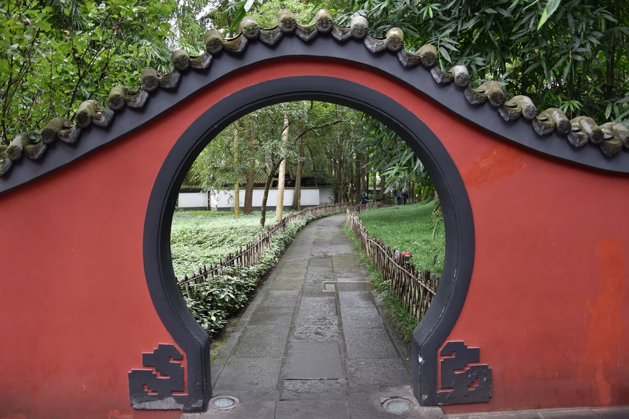 A red moon gate opening onto the bamboo garden path at Du Fu Thatched Cottage Museum in Chengdu.