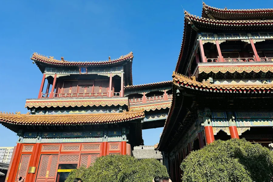 Red halls and layered yellow-glazed roofs inside Beijing's Yonghe Temple set against a deep blue winter sky.