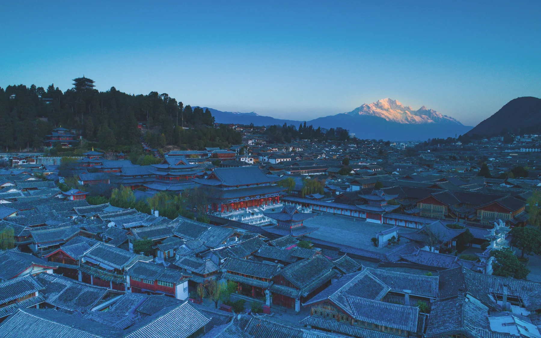Lijiang Old Town rooftops at blue hour with Jade Dragon Snow Mountain catching the last light
