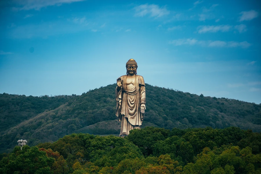 The full bronze Lingshan Grand Buddha rising above a forested mountain near Wuxi under a blue sky.