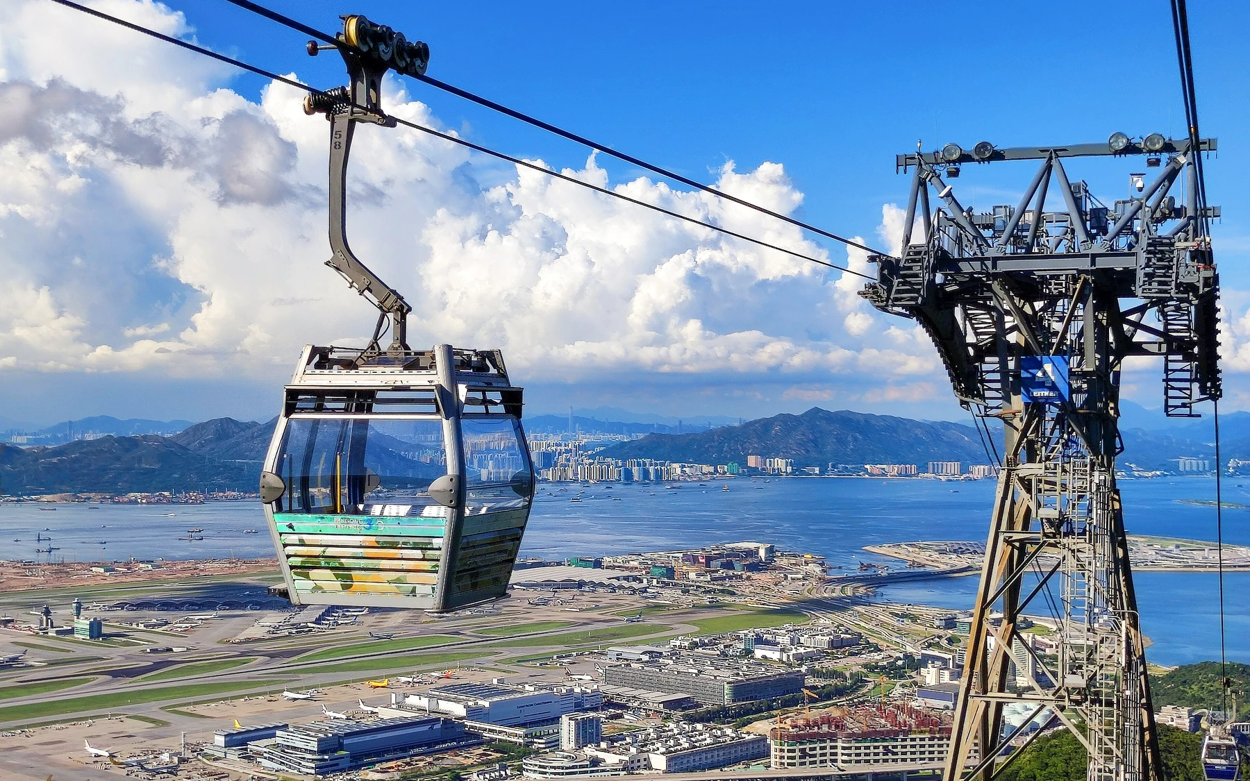 A Ngong Ping 360 cable car above Hong Kong International Airport, Lantau water and distant mountains.