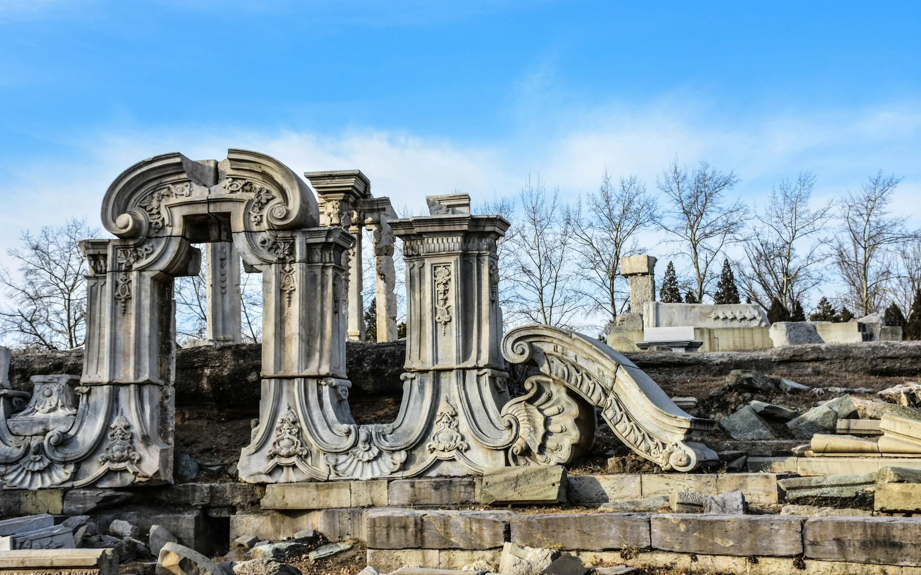 Carved stone arches and architectural fragments from the European Palaces ruins at Beijing's Old Summer Palace beneath a clear blue sky.