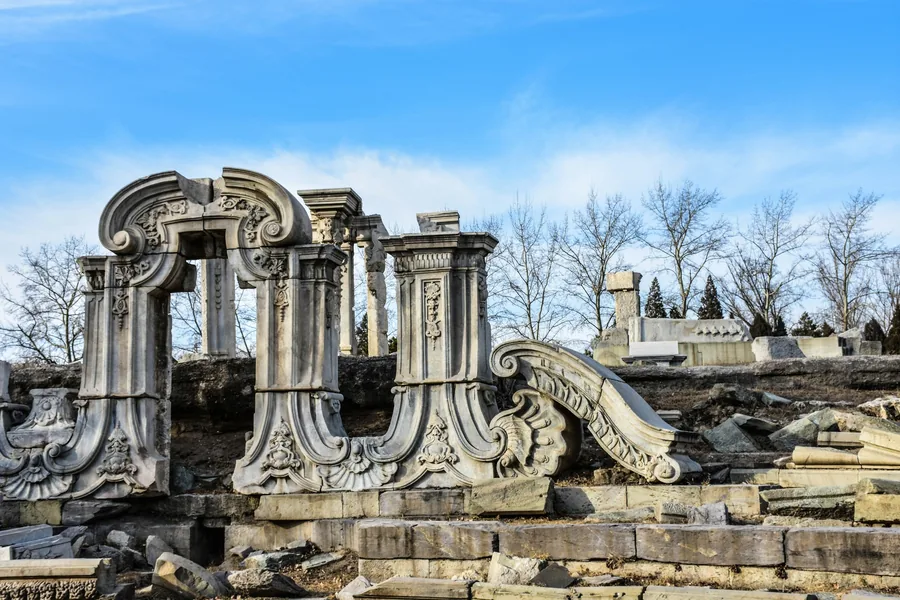 Carved stone arches and architectural fragments from the European Palaces ruins at Beijing's Old Summer Palace beneath a clear blue sky.
