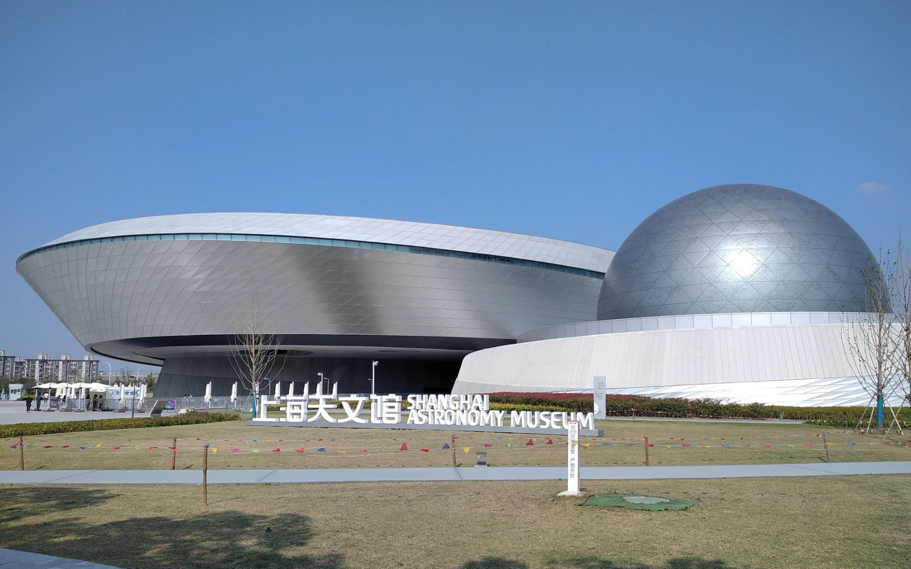 The orbital form, silver dome and bilingual sign of Shanghai Astronomy Museum beneath a clear blue sky