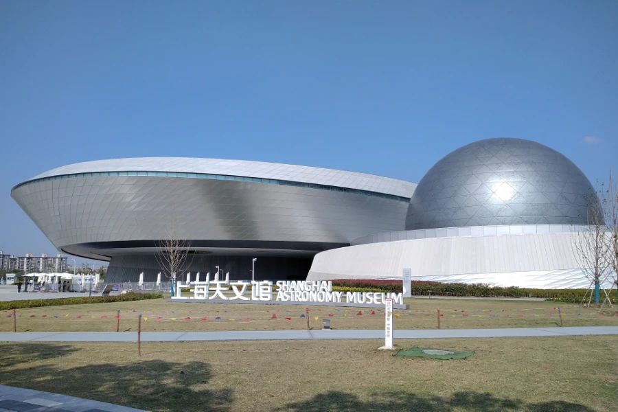 The orbital form, silver dome and bilingual sign of Shanghai Astronomy Museum beneath a clear blue sky