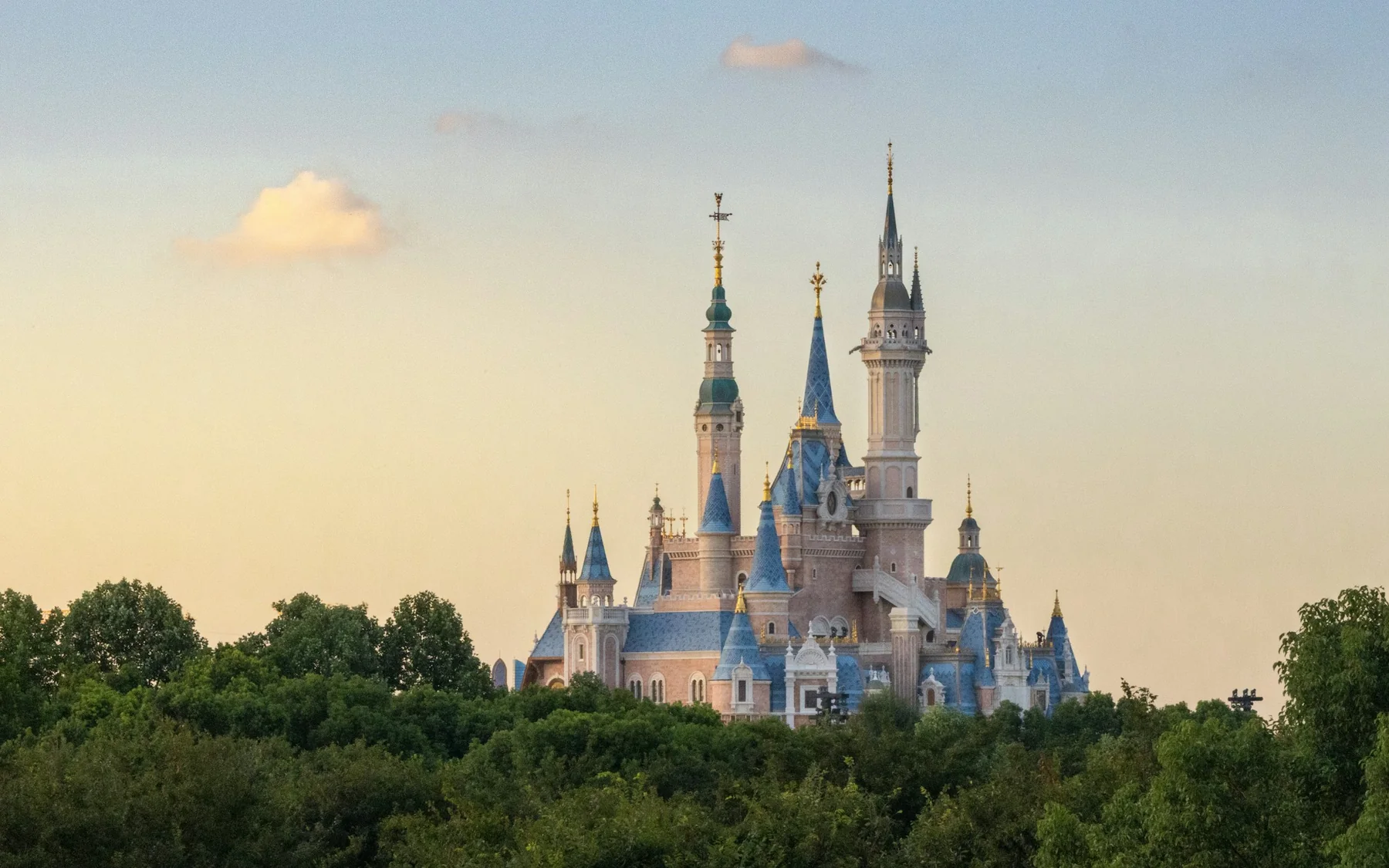Shanghai Disneyland's Enchanted Storybook Castle rising above trees in warm evening light