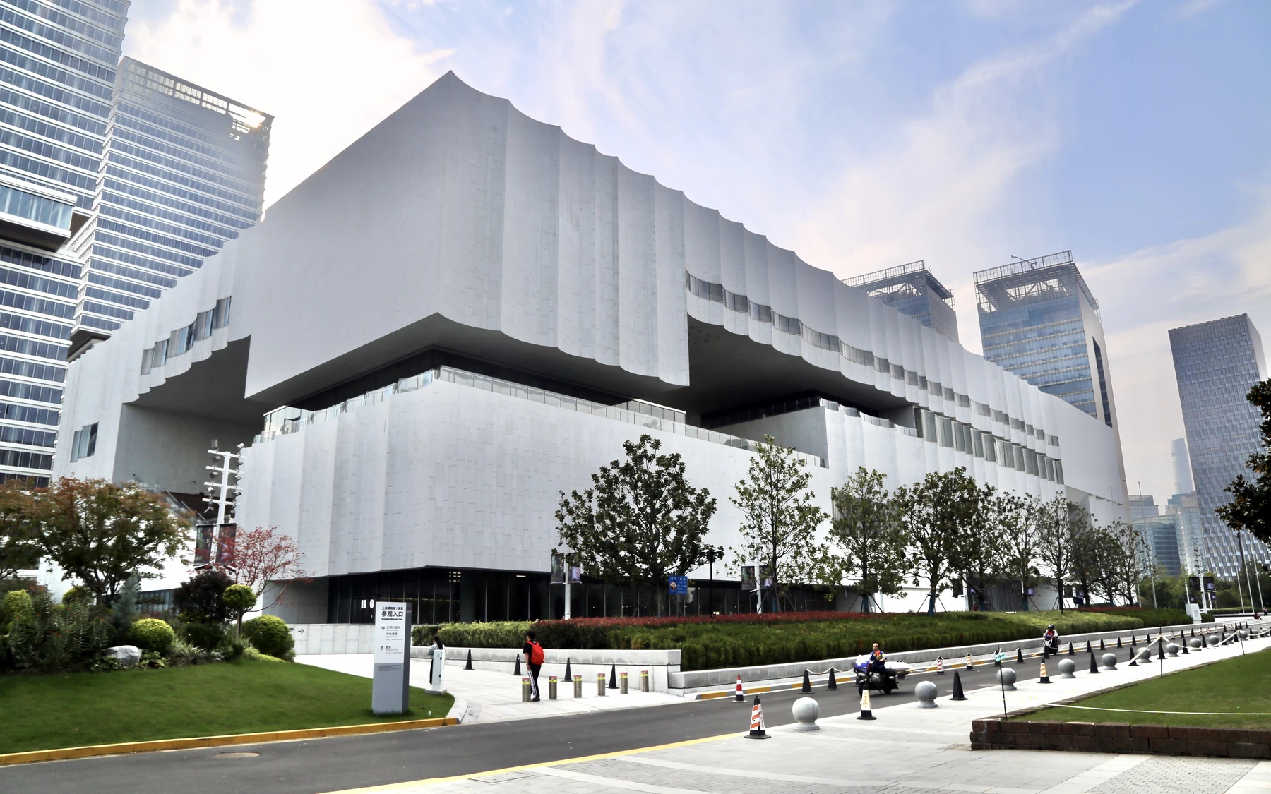 The full white wave-roofed Shanghai Museum East building framed by Pudong towers beneath a clear blue sky