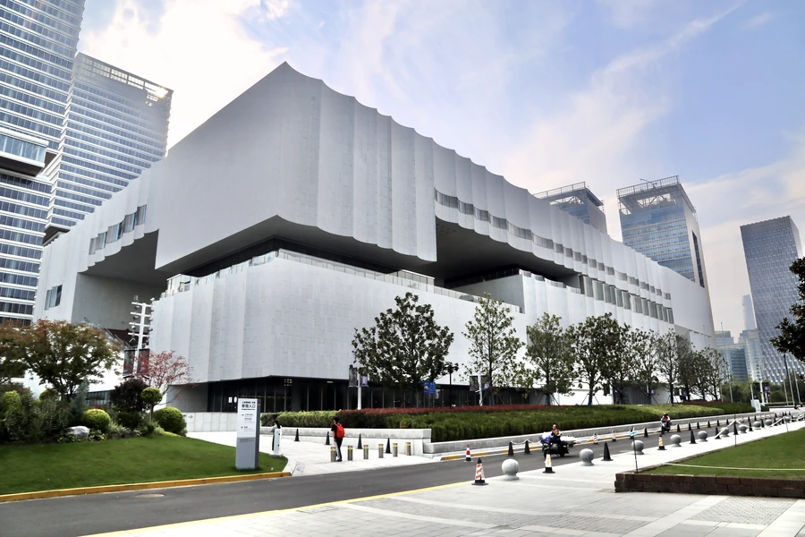 The full white wave-roofed Shanghai Museum East building framed by Pudong towers beneath a clear blue sky