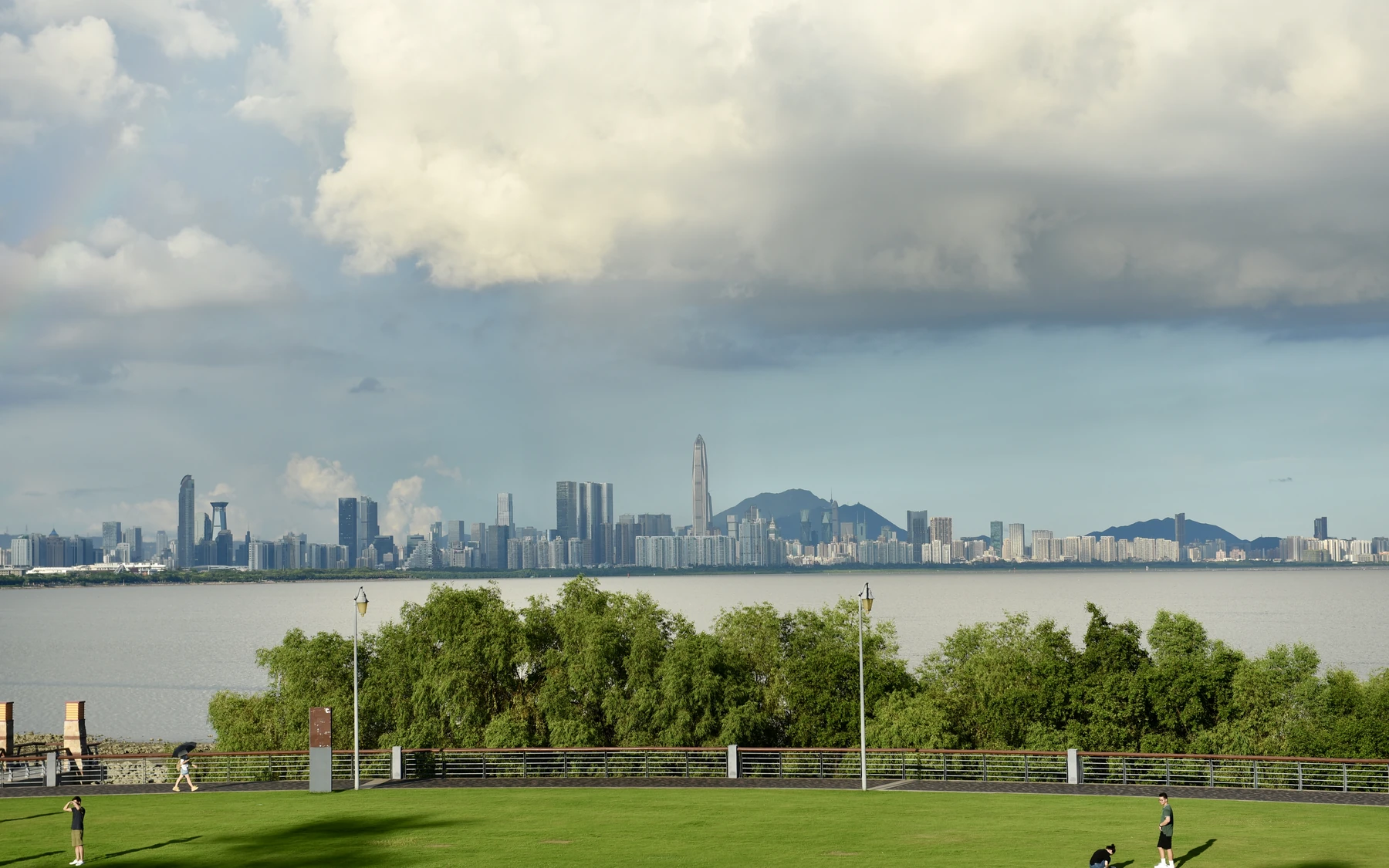 A green lawn and waterfront promenade at Shenzhen Bay Park, with Shenzhen's skyline beyond the bay.