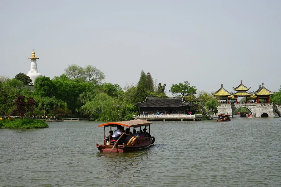 A wooden tour boat crossing Slender West Lake between the White Pagoda and Five-Pavilion Bridge