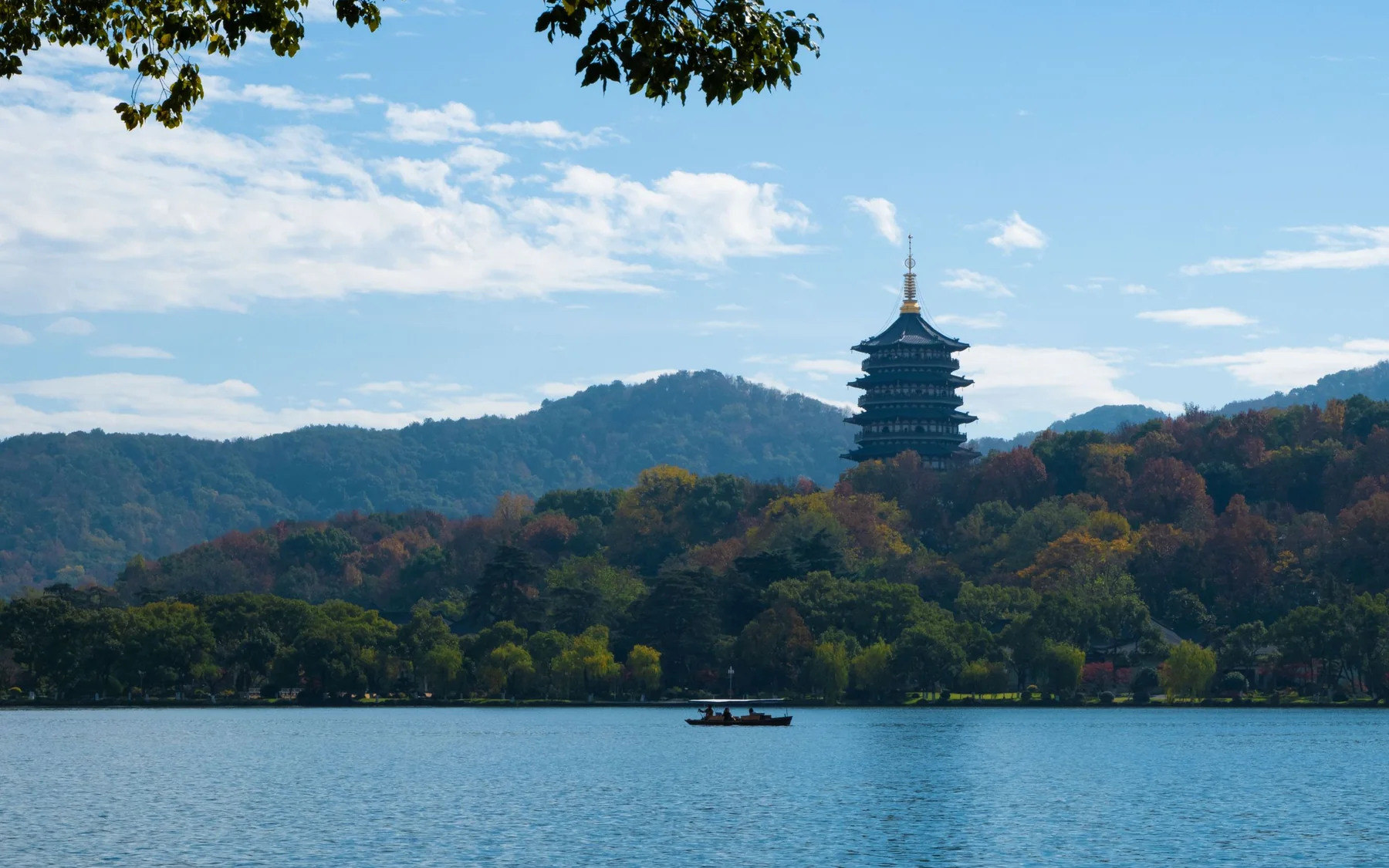 Leifeng Pagoda rising above West Lake with a sightseeing boat in the foreground