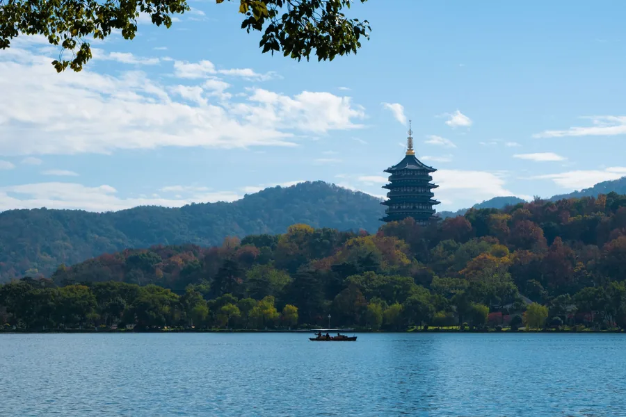 Leifeng Pagoda rising above West Lake with a sightseeing boat in the foreground