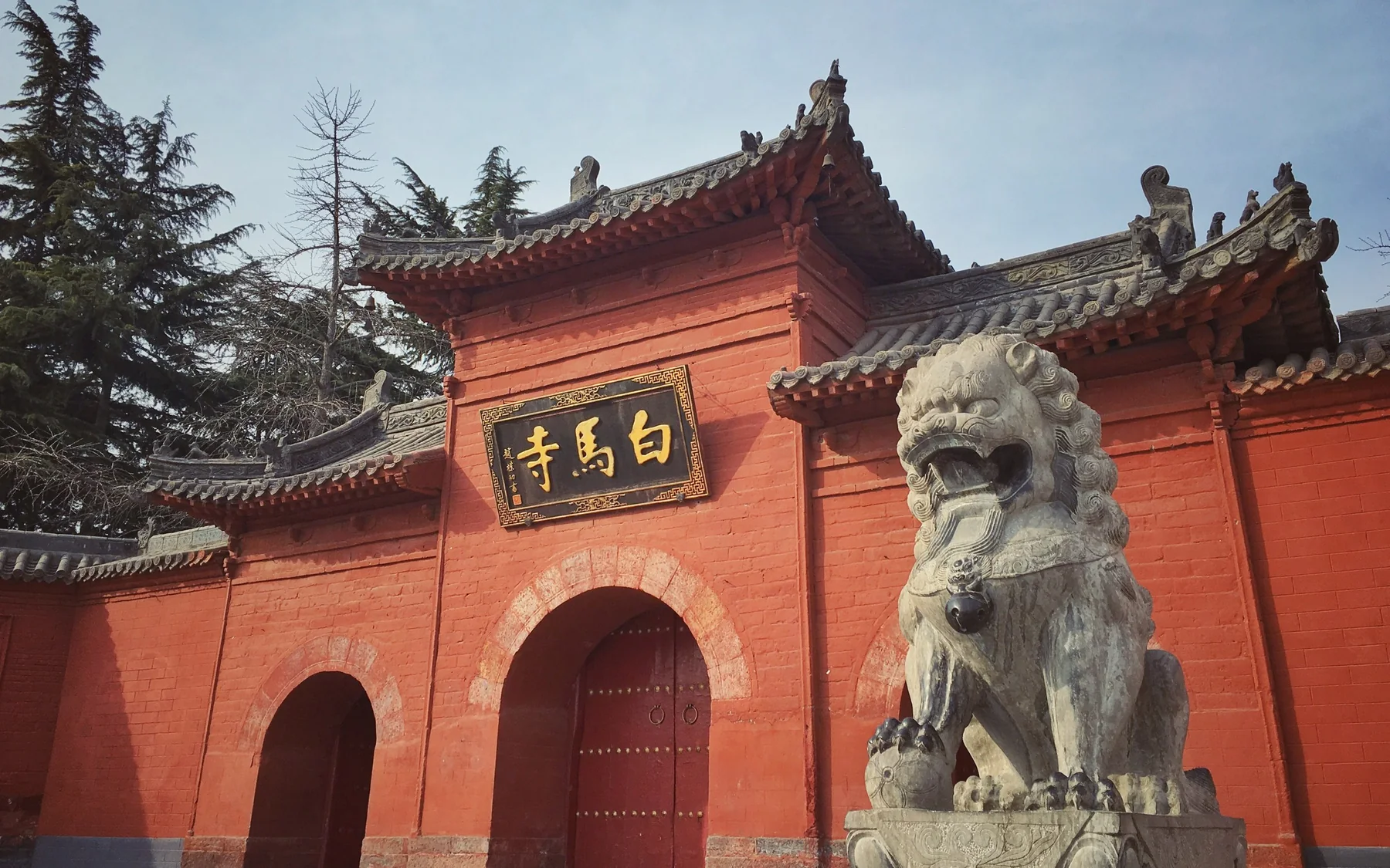 The red-brick shanmen of White Horse Temple in Luoyang, with its gold name plaque and a stone guardian lion in the foreground.
