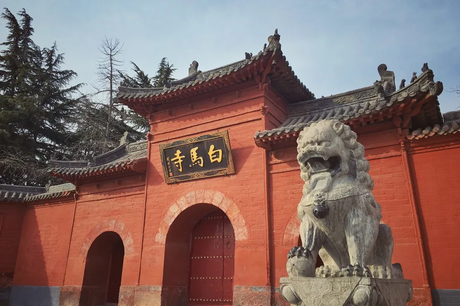 The red-brick shanmen of White Horse Temple in Luoyang, with its gold name plaque and a stone guardian lion in the foreground.
